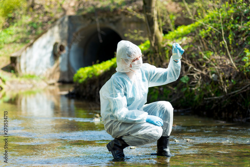 Fotografía a scientist with a test tube takes a sample of water from a sewer discharge