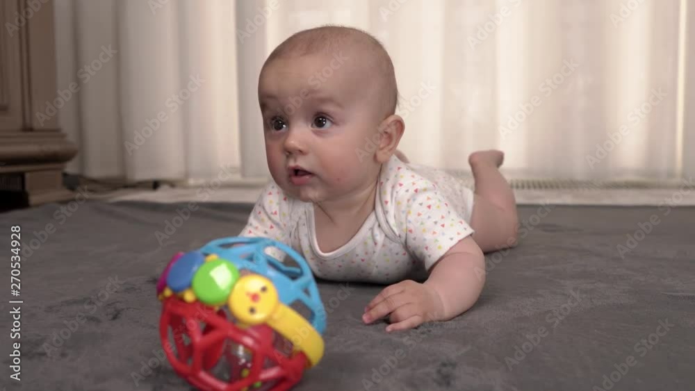 Curious lovely little baby boy playing with colorful ball on the soft carpet at home. First steps in studying new world. Touching moments Curious lovely little baby boy playing with colorful ball on the soft carpet at home. First steps in studying new world. Touching moments