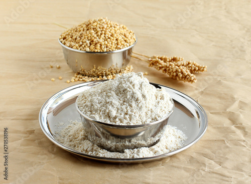 Sorghum flour, a healthy food and that is freshly ground, a whole grain and gluten free, in a steel bowl, and in the background is a bowl of sorghum and its stalk.