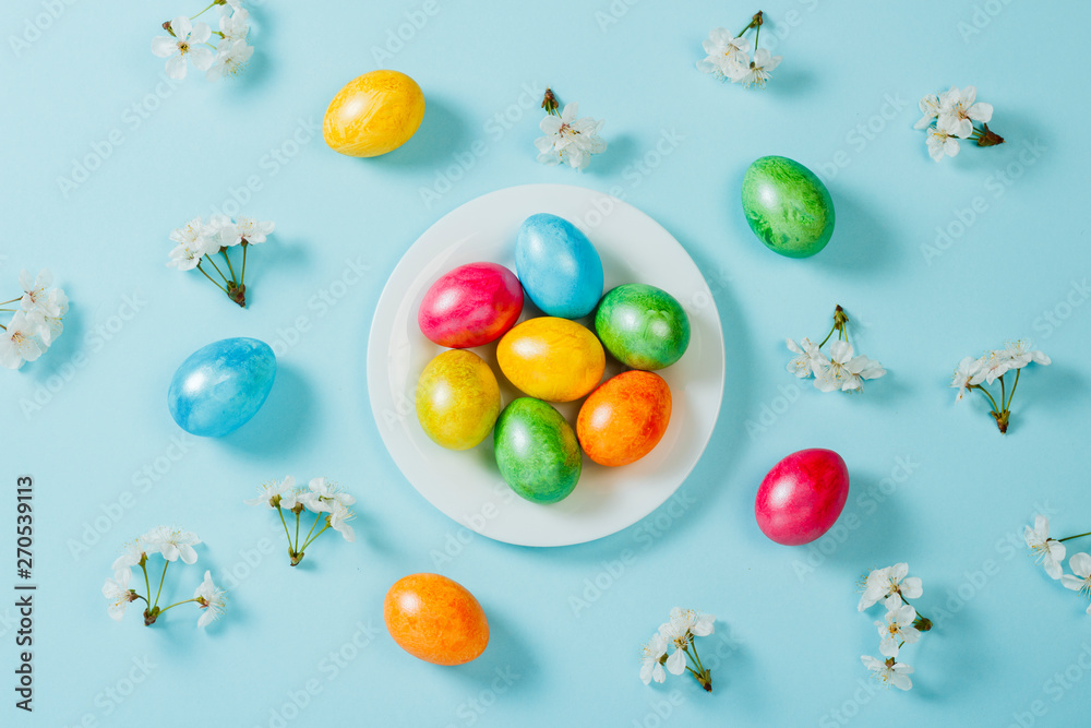 Obraz premium Easter eggs on a plate and spring flowers on a blue background background. Concept of celebrating Easter. Flat lay, top view