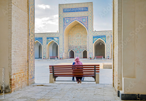 Inner yard of Kalyan Mosque, part of the Po-i-Kalyan Complex, at the sunset. Bukhara, Uzbekistan. A woman in a headscarf sitting on the bench