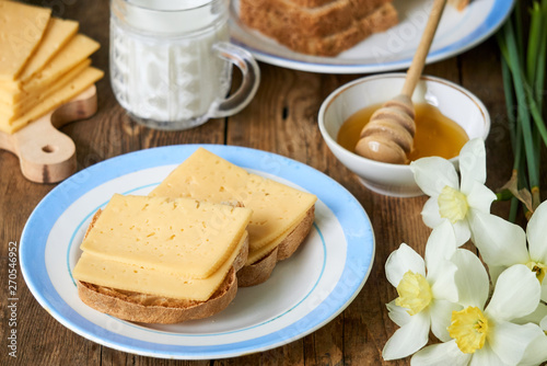 Breakfast with cheese sandwich, milk and honey on a wooden table
