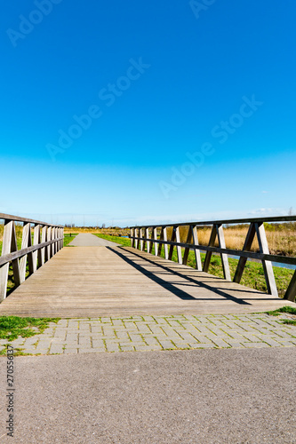 Fototapeta Naklejka Na Ścianę i Meble -  hiking path and wooden bridge in recreation park Zuidpolder in Barendrecht, The Netherlands. Blue sky, copy space