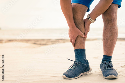 Man runner hold his sports injured leg on the beach background