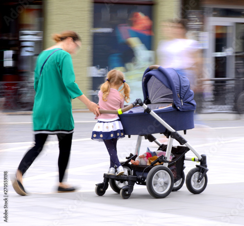 Young mother with small child in the stroller walking down the s