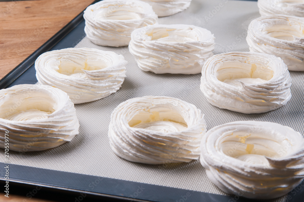 Round-shaped meringues on baking sheet. Close-up of baked crispy dessert. Recipe concept