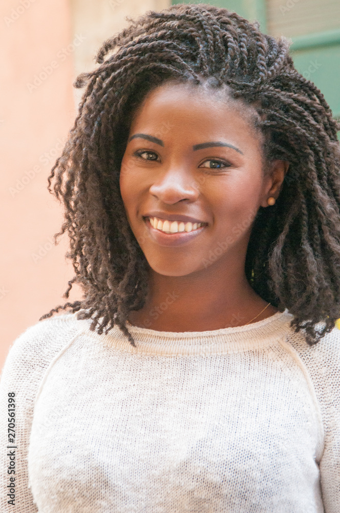 Positive cheerful Afro American student girl smiling at camera. Happy black woman standing for camera outdoors. Female portrait concept