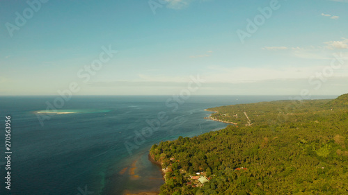 Seascape island coast with forest and palm trees, coral reef with turquoise water, aerial view. Coastline of tropical island covered with green forest against the blue sky with clouds and blue sea