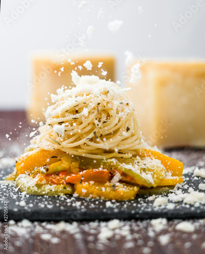 Falling cheese over spaghetti pasta with vegetables.