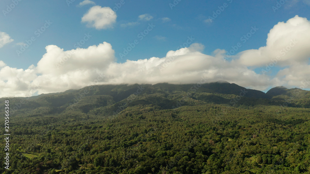 Mountain landscape on tropical island with mountain peaks covered with forest from above. Mountains covered rainforest, trees and blue sky with clouds, aerial view. Camiguin, Philippines. Slopes of