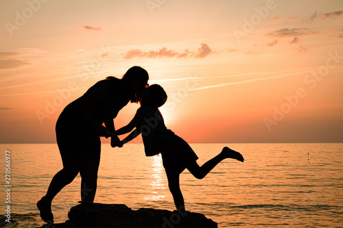 silhouettes of mom with daughter. mother and daughter kiss at sunset.