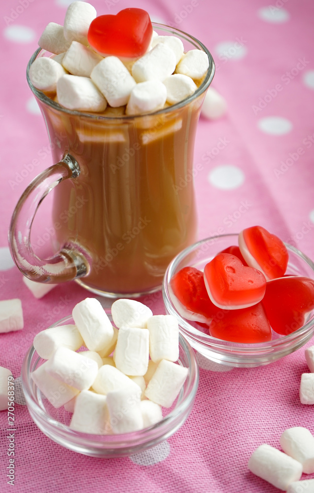 breakfast. transparent small Cup of coffee with milk, decorated with a small marshmallow with a heart of marmalade, on a background of pink tablecloth with white circles
