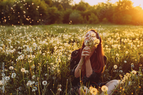young woman with dandelions in hand in a field against the evening sun. sunset. joy. smile