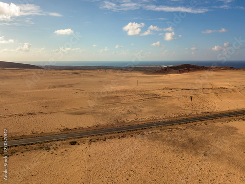 Aerial view of a desert landscape on the island of Lanzarote  Canary Islands  Spain. Road that crosses a desert. Tongue of black asphalt cutting a desert land. Reliefs on the horizon. Volcanoes