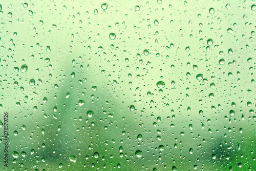 Rain drops on window with green tree as background. Natural water drops on glass. Selective focus