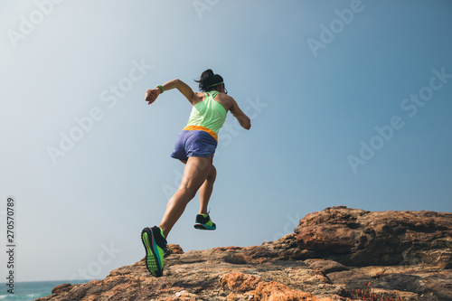 Woman trail runner running to rocky mountain top on seaside