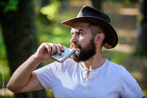 Hipster with beard drink alcohol nature background defocused. Hiking camping. Wanderer concept. Alcohol drink. Nomadic man carry alcohol with him. Guy brutal bearded cowboy drink alcohol metal flask