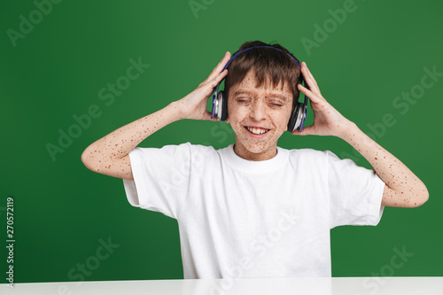 Happy young boy with freckles in headphones listening music