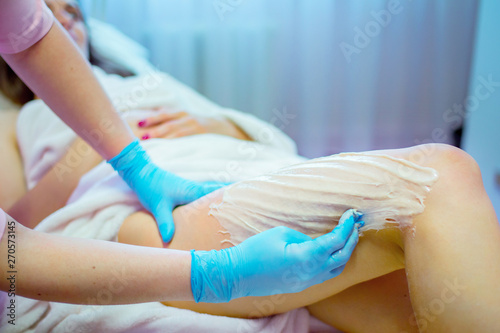 Close-up hands of cosmetologist in blue gloves applying paste for sugaring depilation on woman leg, hair removal beauty procedure.