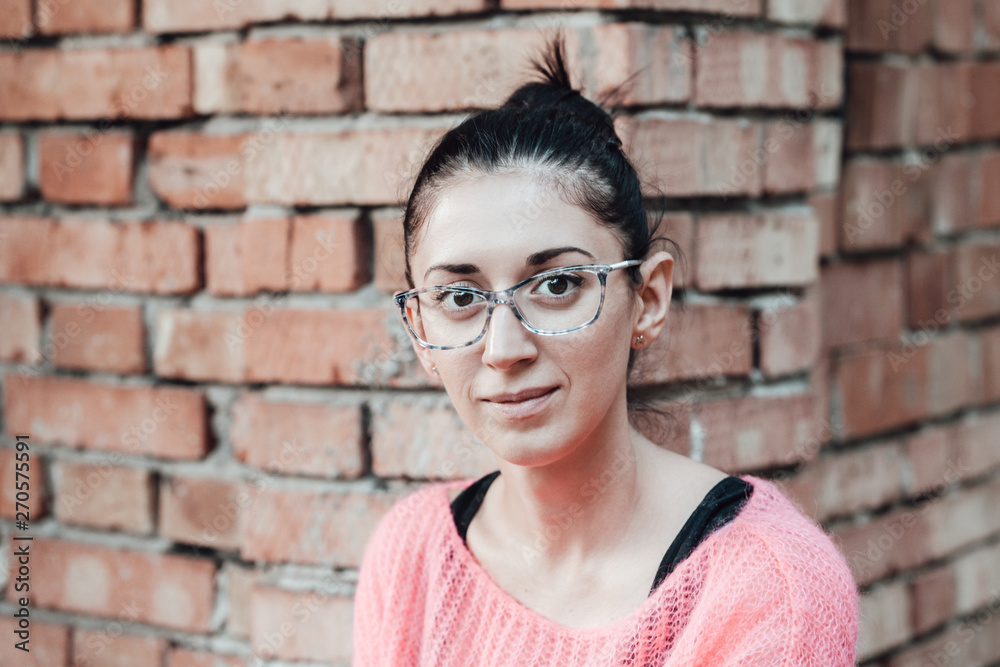 Portrait of a beautiful young woman with glasses on a brick wall background.
