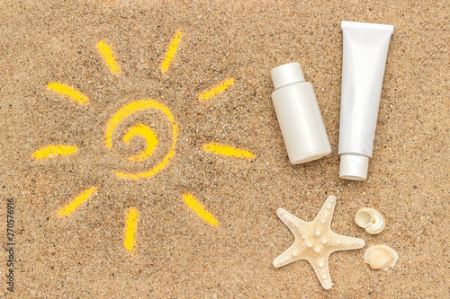 Sun sign drawn on sand, starfish and white tube, bottle of sunscreen. Template mockup for your design. Creative top view