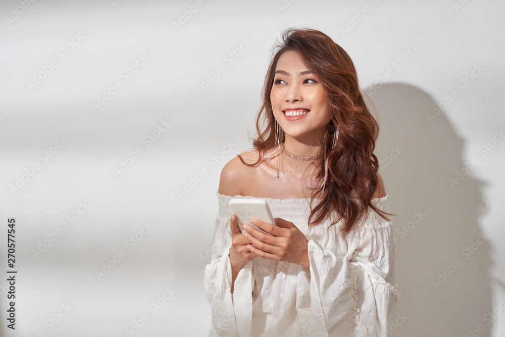 a smiling attractive asian woman texting on mobile phone while standing isolated over white background a smiling attractive asian woman texting on mobile phone while standing isolated over white background