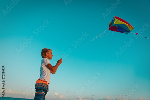 Young boy flying a kite on tropical beach at sunset