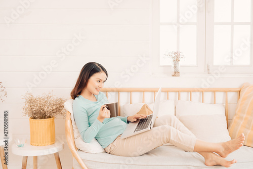 Happy casual beautiful woman working on a laptop sitting on the sofa in the house.