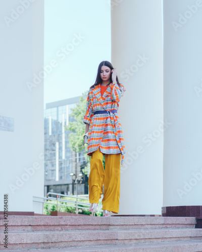 The girl in beautiful and fashionable clothes. Posing at the columns of the theater.