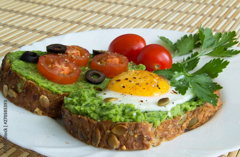 Sandwich with guacamole, egg, olives and tomatoes on a plate