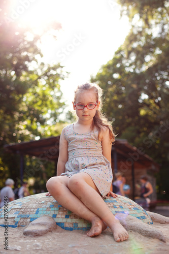 young girl with glasses plays on the playground, sunny day.
