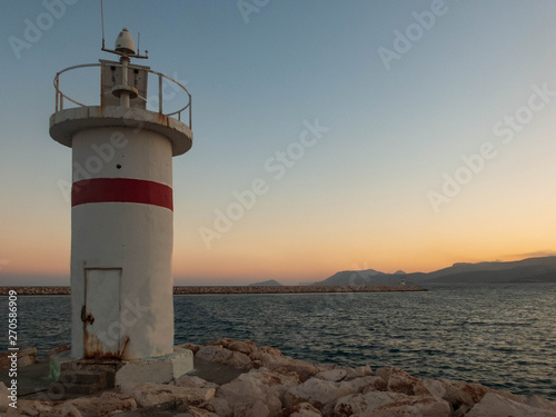 Lighthouse on the stone pier  sea harbor and hills at the sunset