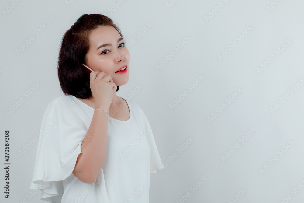 Asian beautiful woman Standing in a white shirt Put the mobile phone attached to the ear to talk to the destination. Prepare to make a call. With a happy smile With a white background Asian beautiful woman Standing in a white shirt Put the mobile phone attached to the ear to talk to the destination. Prepare to make a call. With a happy smile With a white background