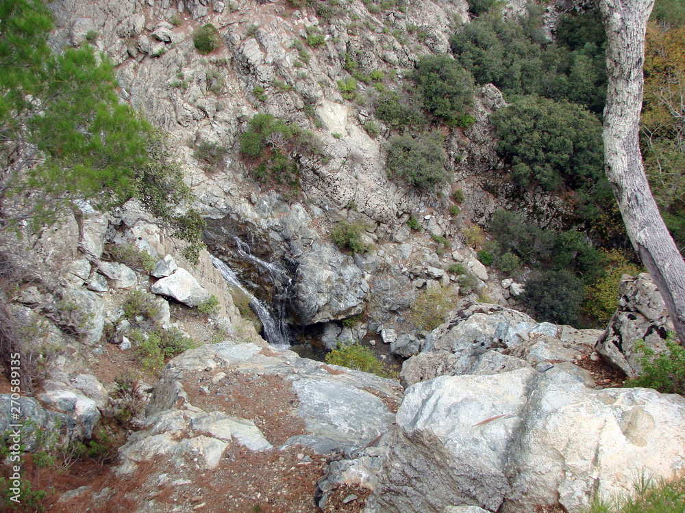 Panorama of the rocky surface of the slope of the mountain range, through which stones break through the rapid flow of an underground mountain river. Panorama of the rocky surface of the slope of the mountain range, through which stones break through the rapid flow of an underground mountain river.