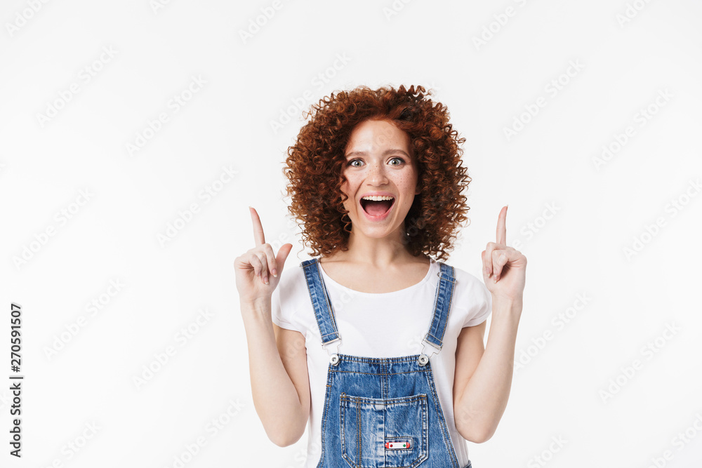 Curly happy redhead girl posing isolated over white background pointing. Curly happy redhead girl posing isolated over white background pointing.