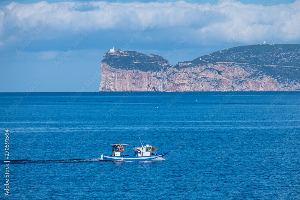 View of Capo Caccia from Alghero (L'Alguer),  as fishing boat entere the harbor, Sardinia, Italy.  Famous for the beauty of its coast and beaches and its historical city center.
