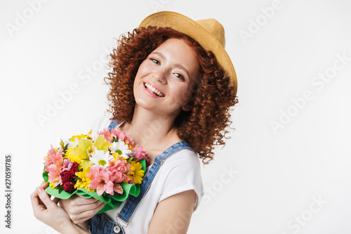 Portrait of cheery redhead curly woman 20s wearing summer straw hat smiling and holding flower box