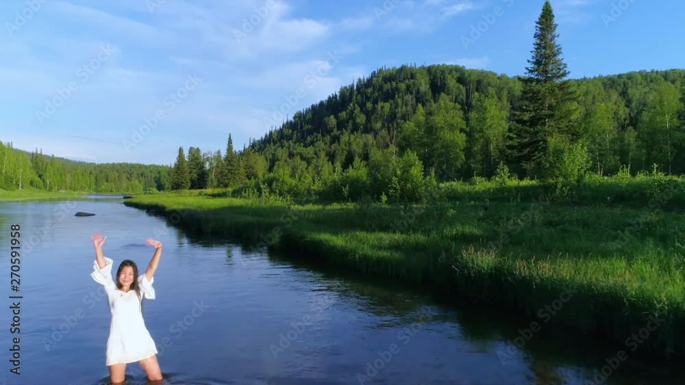 girl walks in the water on a mountain river, arms outstretched, with joy. Asian stands in the river and plays with water. whirlwinds and splashes of water, the girl in the river. slow motion. Aerial.