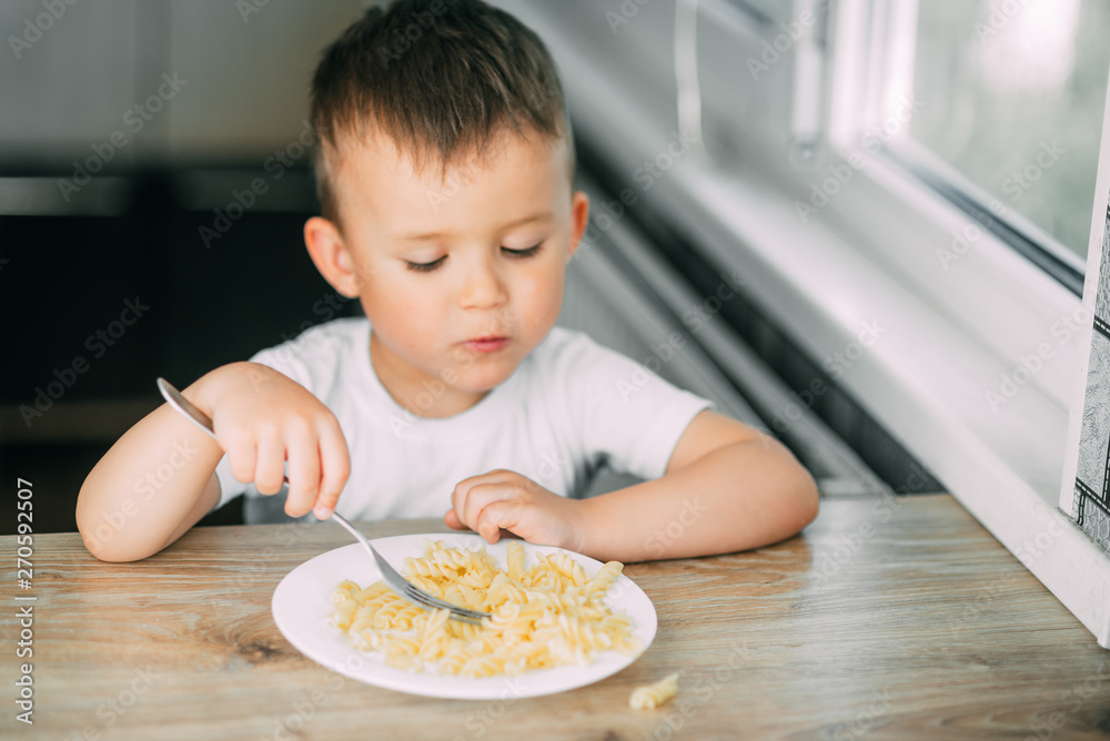 a little boy eats pasta in the form of a spiral in the afternoon in the kitchen on their own a little boy eats pasta in the form of a spiral in the afternoon in the kitchen on their own
