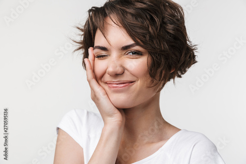 Portrait of positive woman with short brown hair in basic t-shirt smiling and touching her face with hand
