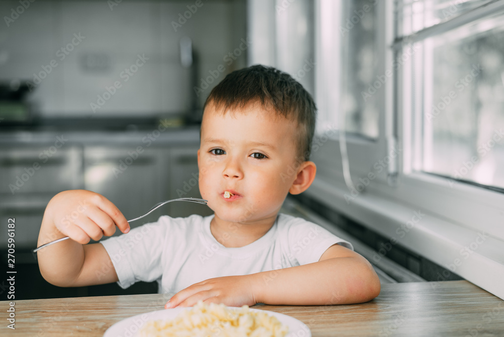 little boy eats pasta in the form of a spiral in the afternoon in the kitchen on their own little boy eats pasta in the form of a spiral in the afternoon in the kitchen on their own