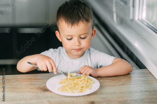 little boy eats pasta in the form of a spiral in the afternoon in the kitchen on their own