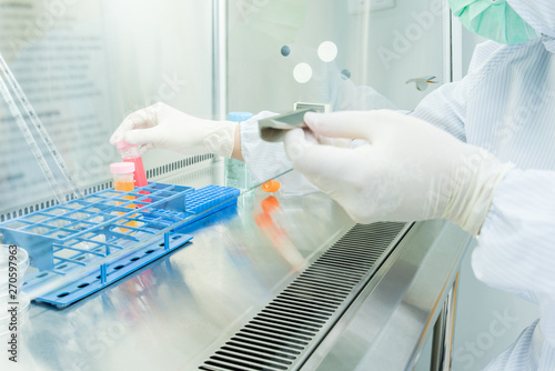 A scientist in sterile coverall gown preparing growth medium and reagent for cell cuture assay in biological safety cabinet (BSC). Doing molecular experiment in cleanroom facility. photo