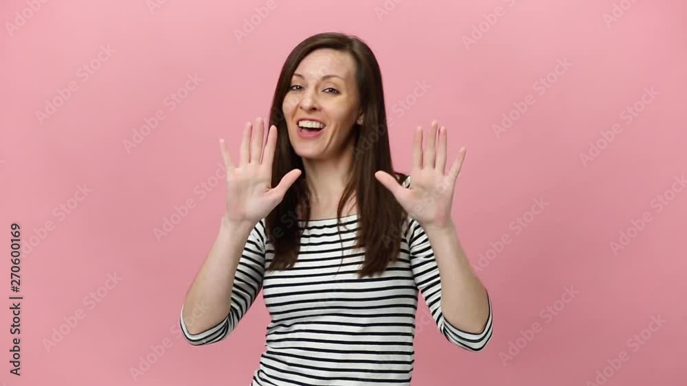 Joyful pretty brunette young woman in striped shirt, fooling, dancing, looking at camera with charming smile isolated over pastel pink background in studio. People sincere emotions lifestyle concept Joyful pretty brunette young woman in striped shirt, fooling, dancing, looking at camera with charming smile isolated over pastel pink background in studio. People sincere emotions lifestyle concept
