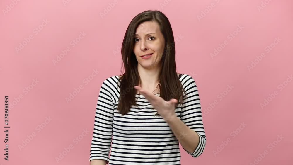 Perplexed pretty confused pensive brunette young woman in striped shirt looking camera, aside, gesticulating isolated over pastel pink background in studio. People sincere emotions, lifestyle concept. Perplexed pretty confused pensive brunette young woman in striped shirt looking camera, aside, gesticulating isolated over pastel pink background in studio. People sincere emotions, lifestyle concept.