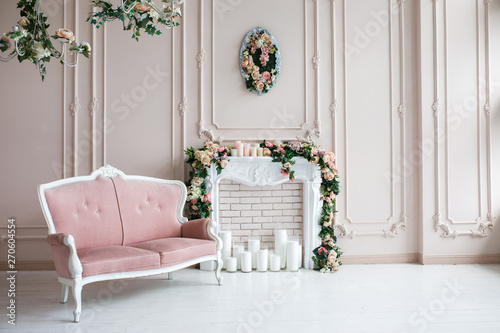 Elegant white fireplace full of flowers. Elegant white room with a sofa. Wedding area. Vintage decor in a bright interior
