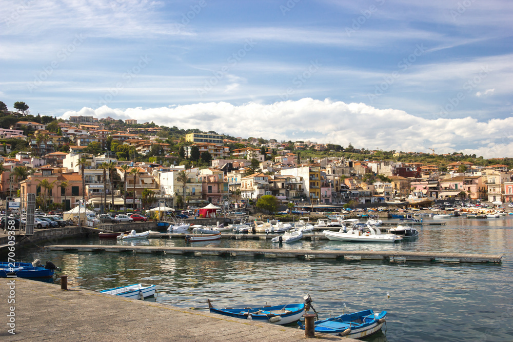 Acitrezza Sicily, view of the tourist harbor, fishing boats, houses of the town and blue sky