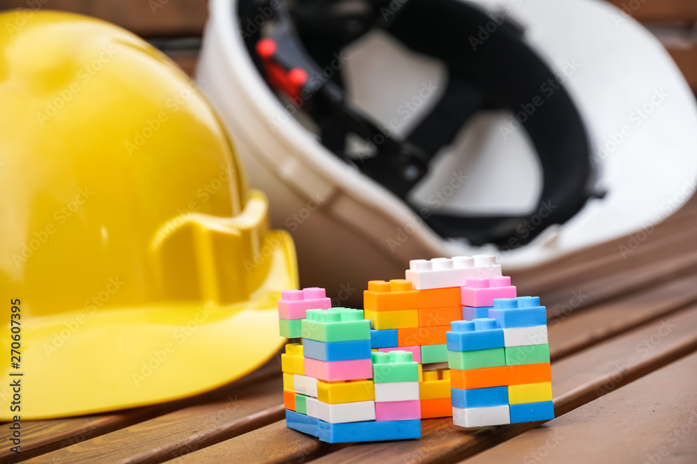 Fototapeta premium Real estate and new house construction concept. Protective hardhats, and multicoloured plastic construction building blocks or toy bricks. Selective focus