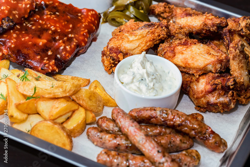Dish of mixed meats. Grilled ribs, chicken wings and sausages with French fries