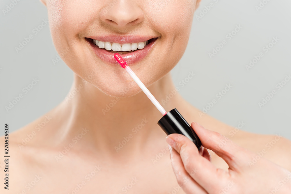 cropped view of cheerful naked woman applying lip gloss and smiling isolated on grey